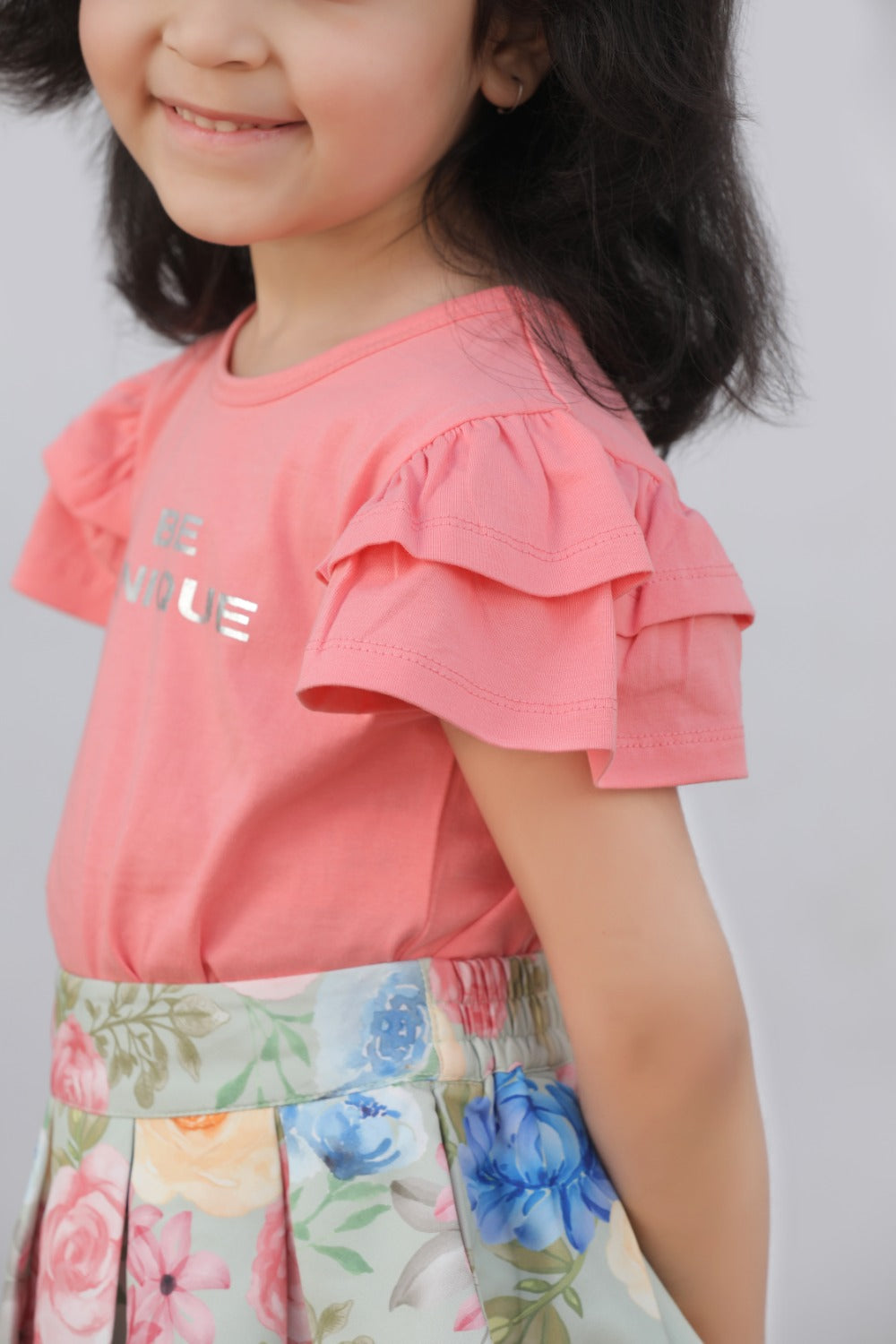 Side view of girl in coral ruffle top and floral flared skirt