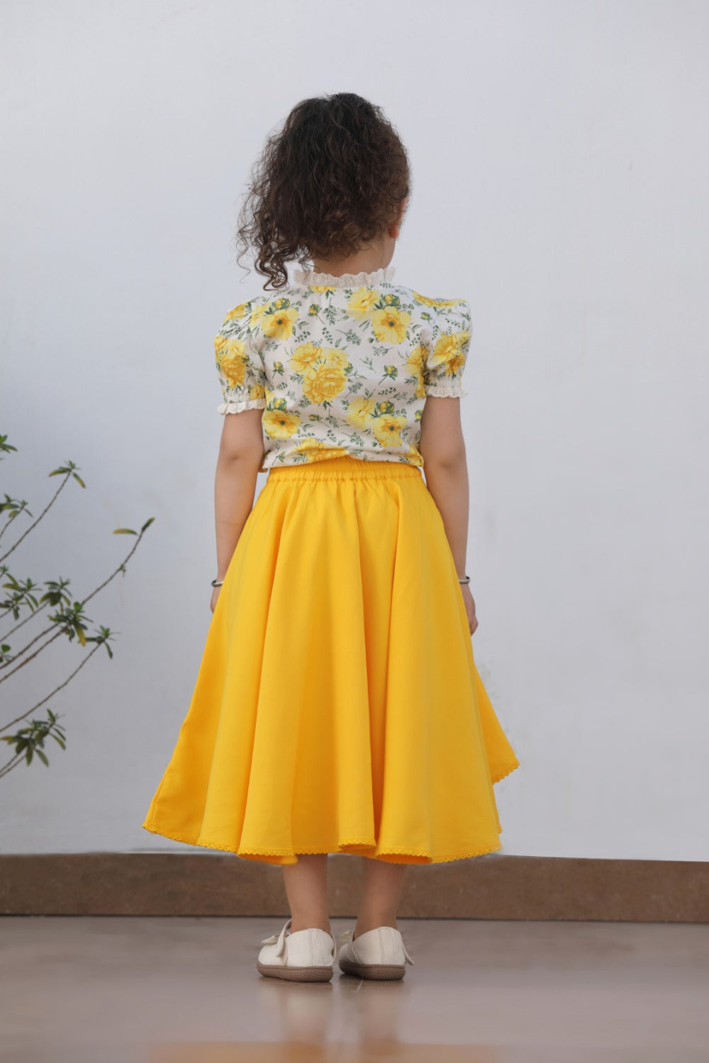 Back view of girl in white floral top and yellow asymmetric flared skirt