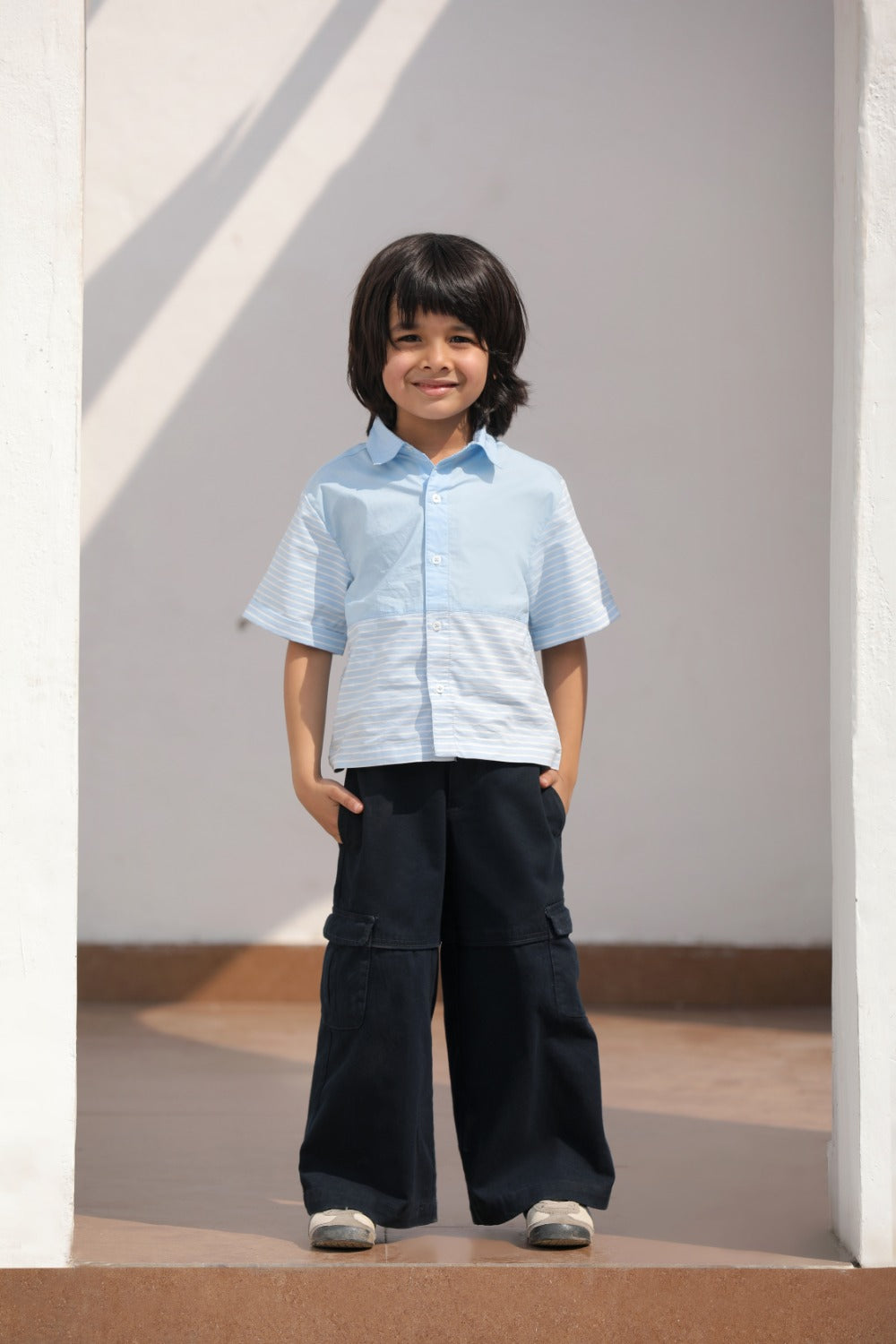 Luxe & Hardy Ash Blue Panelled Shirt – three-quarter view of light blue panelled texture short sleeve boys shirt, kids ethnic casual party wear shirt, styled with navy blue cargo pants and sneakers