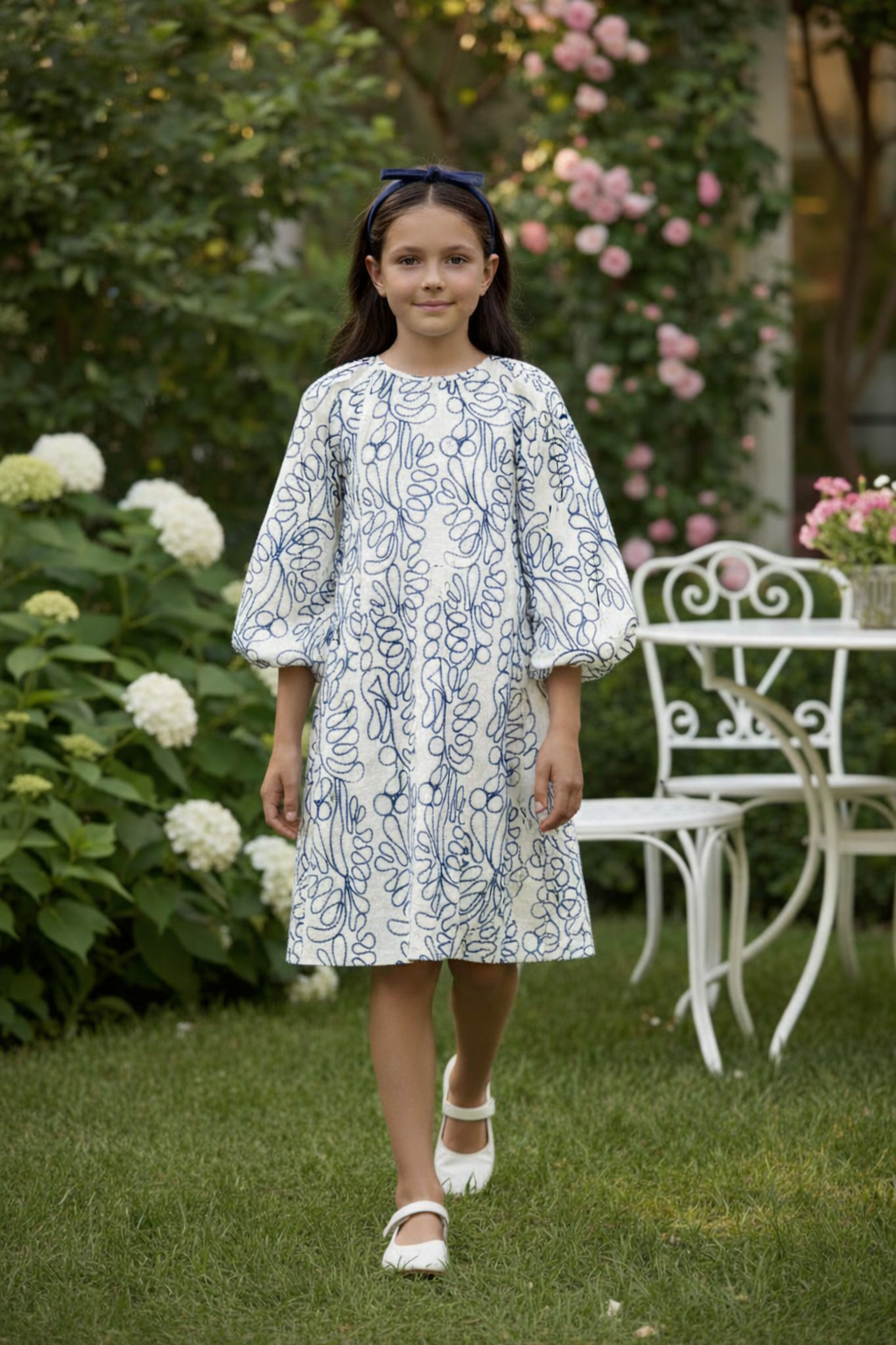 Side view of girl in white and blue block-print dress walking in garden