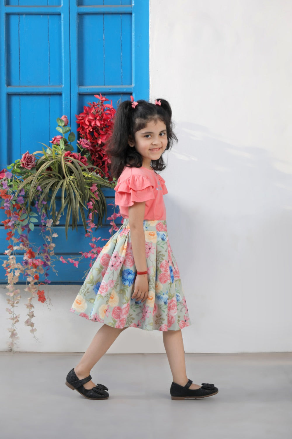 Girl in coral top and floral skirt posing outdoors near a blue door