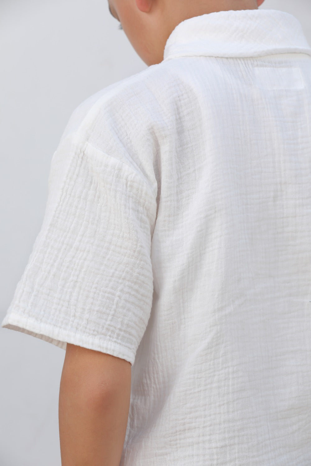 Luxe & Hardy Milo Textured Tee – three-quarter view of white textured linen short sleeve boys shirt, kids ethnic party wear casual shirt, styled with sage green wide leg pants and white sneakers